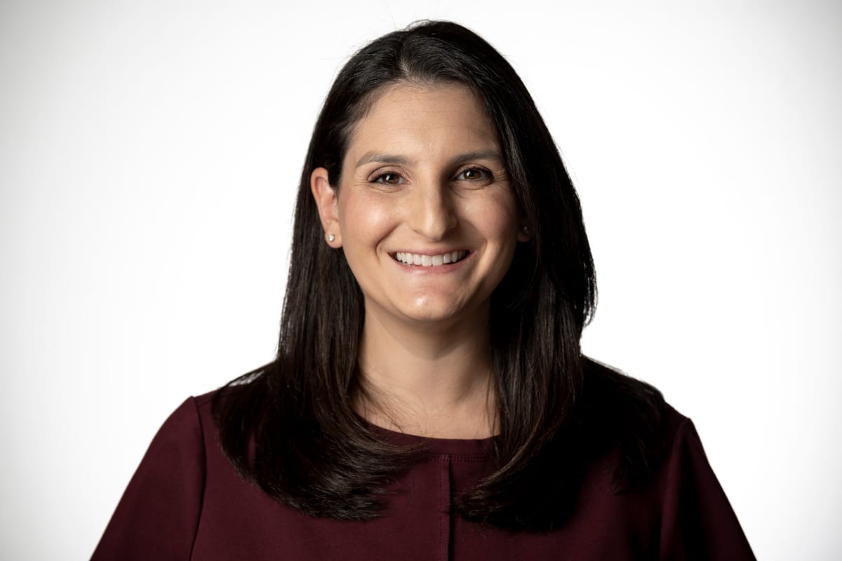 A woman with long dark hair and a maroon top is smiling at the camera against a plain white backdrop.