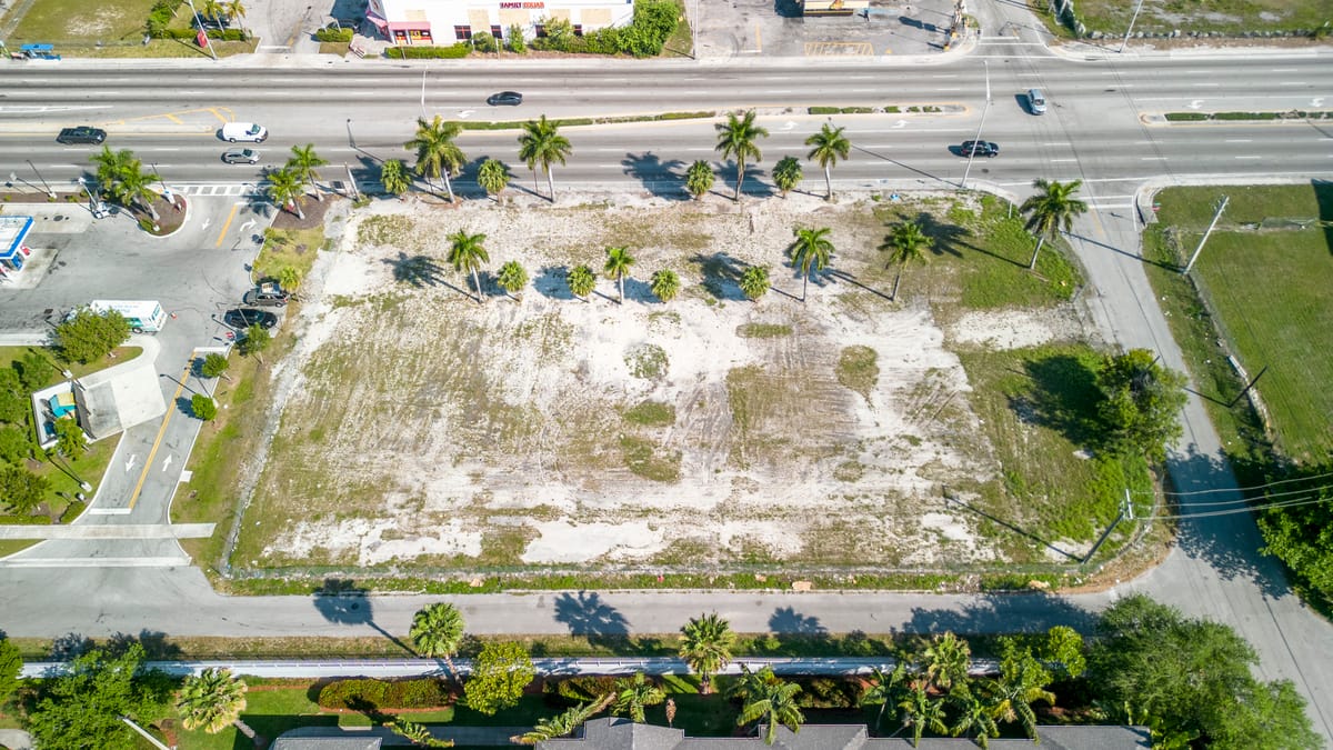 Aerial view of a vacant lot with palm trees and a road running along its edge.