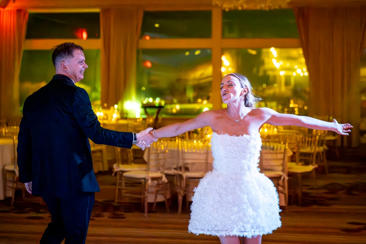 A man and woman dancing in a ballroom, holding hands and smiling.