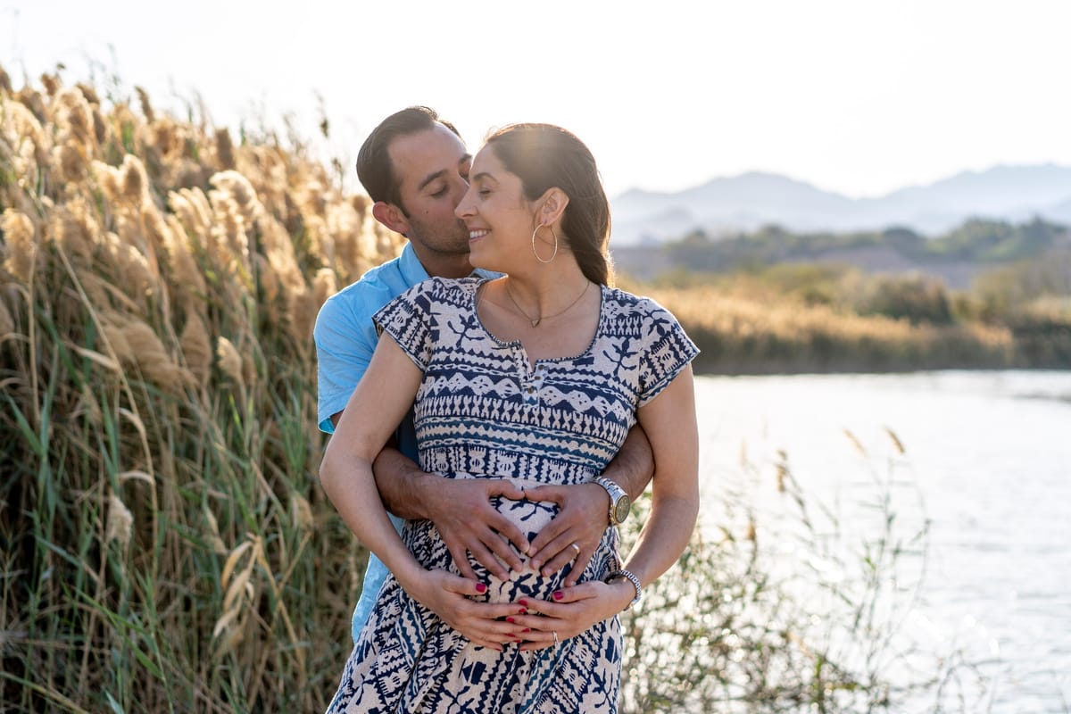 A man and woman stand together, embracing, with their hands on the woman's pregnant b
