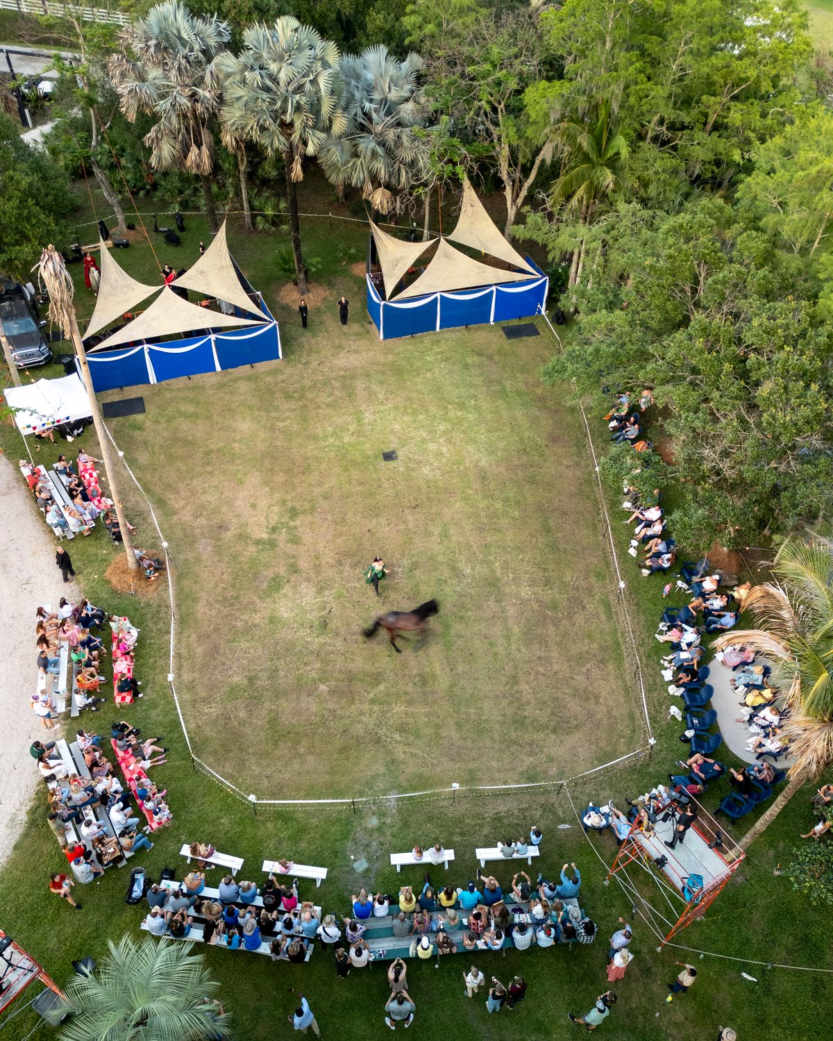 Aerial view of an outdoor event with a crowd of people gathered around a stage or performance area.