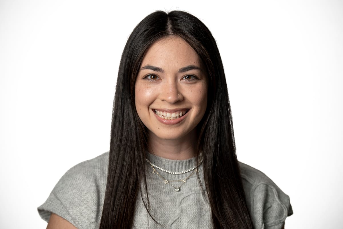 A young woman with long dark hair and a gray shirt smiles at the camera.